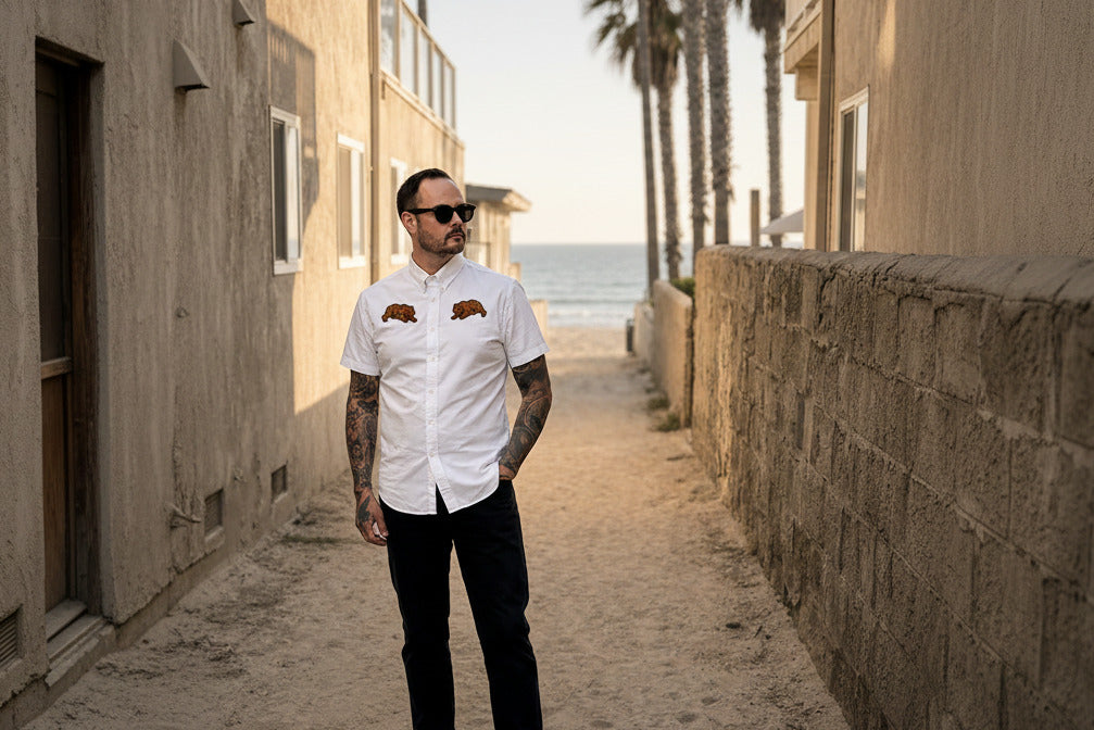 Man wearing a white shirt with bear emblems on a beachside path.
